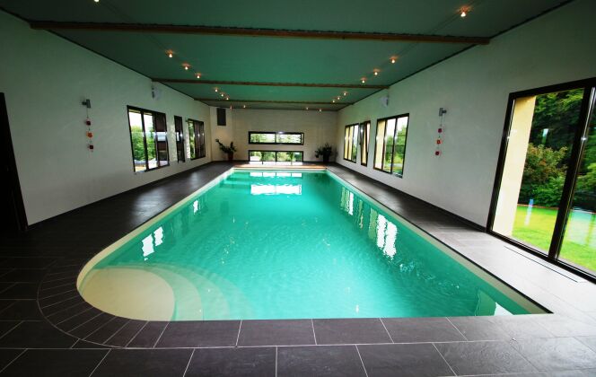 Couloir de nage intérieur avec escalier d'angle arrondi et plages de carrelage noir © L'Esprit Piscine