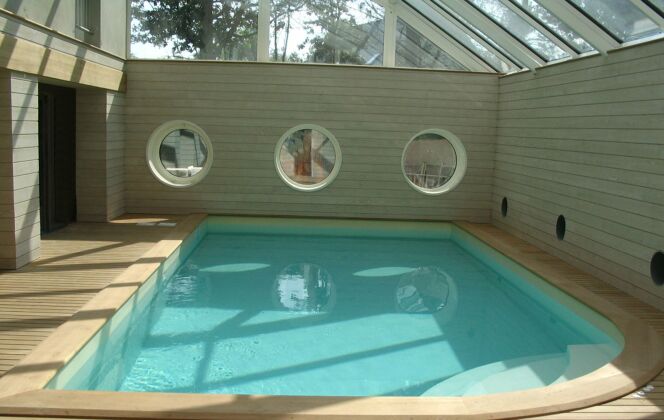 Piscine intérieure avec escalier d'angle arrondi, plages de bois clair et fenêtres hublots © L'Esprit Piscine