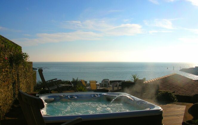 Spa extérieur avec solarium de bois, vue sur mer et lumière de fin de journée. © L'Esprit Piscine