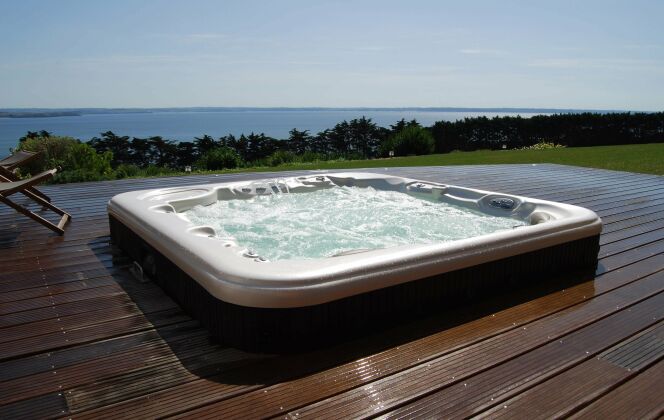 Spa extérieur avec grand solarium de bois et vue sur mer. © L'Esprit Piscine